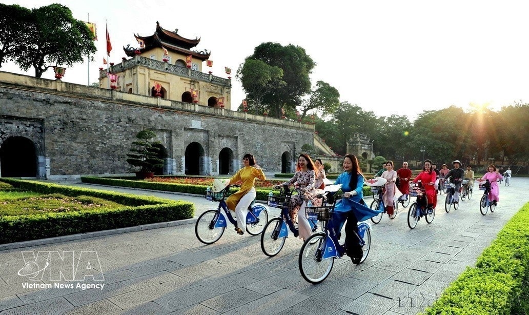 Phụ nữ Thủ đô trong trang phục áo dài đạp xe qua Hoàng thành Thăng Long - Di sản Văn hóa Thế giới của Hà Nội được UNESCO công nhận. Ảnh: TTXVN