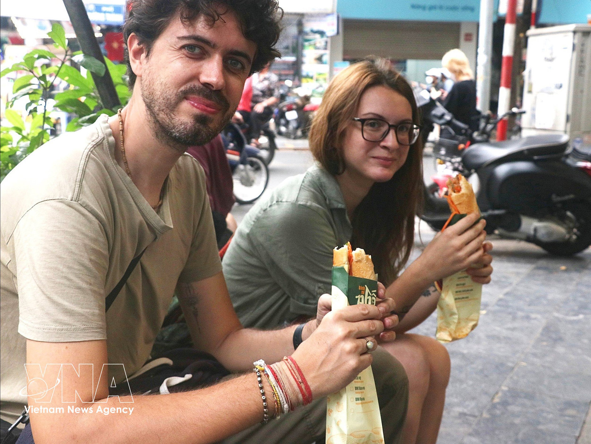 Du khách nước ngoài ăn bánh mì trên vỉa hè Hà Nội. Ảnh: TTXVN